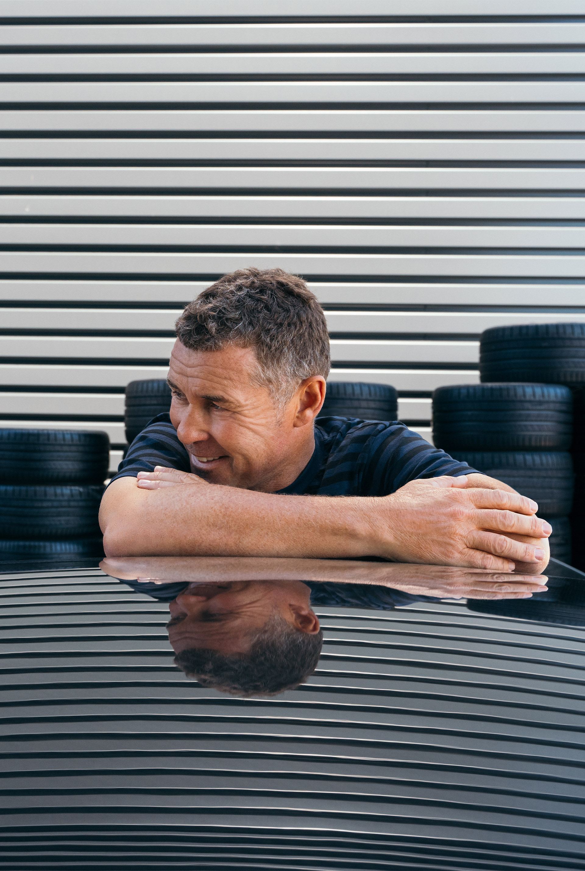 Tom Kristensen leans relaxed against the car and smiles mischievously to the side.